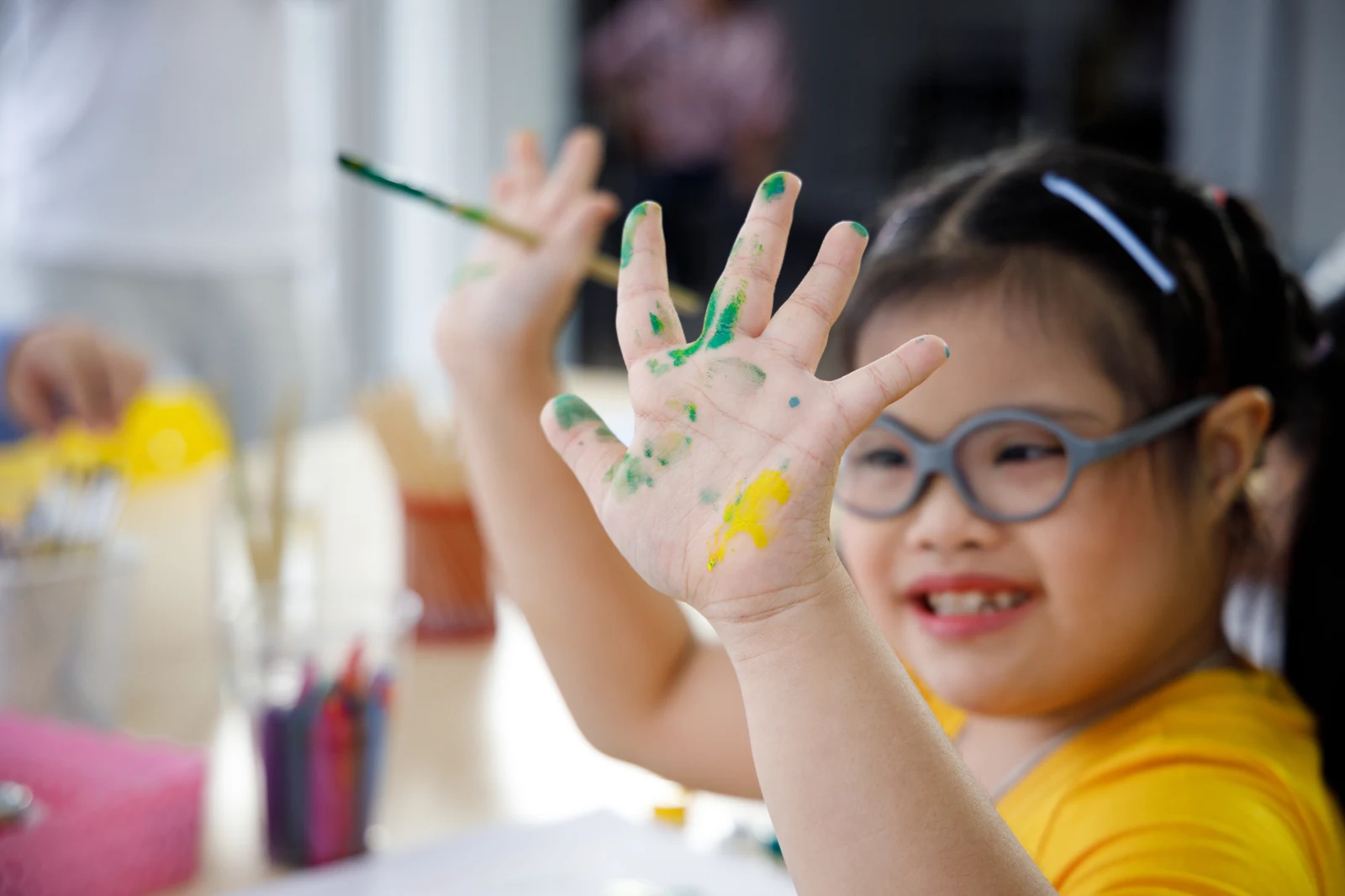 A child smiling and showing a colorful painted hand during an art activity