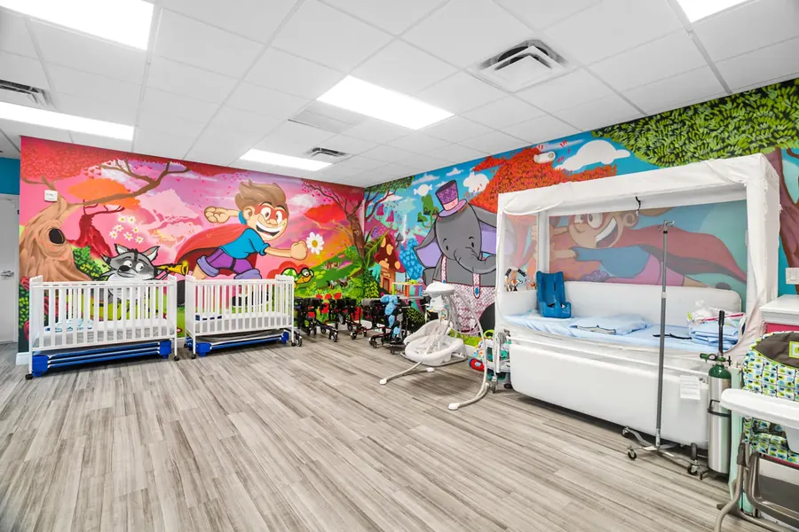 The medical care area at Superhero Kids PPEC, with cribs, a care bed and a painted mural