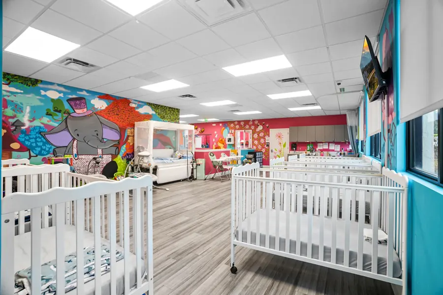 The infant care room at Superhero Kids PPEC, with white cribs and a painted elephant mural
