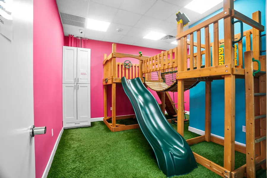 The indoor playground at Superhero Kids PPEC, with a green slide, a rope bridge and artificial grass
